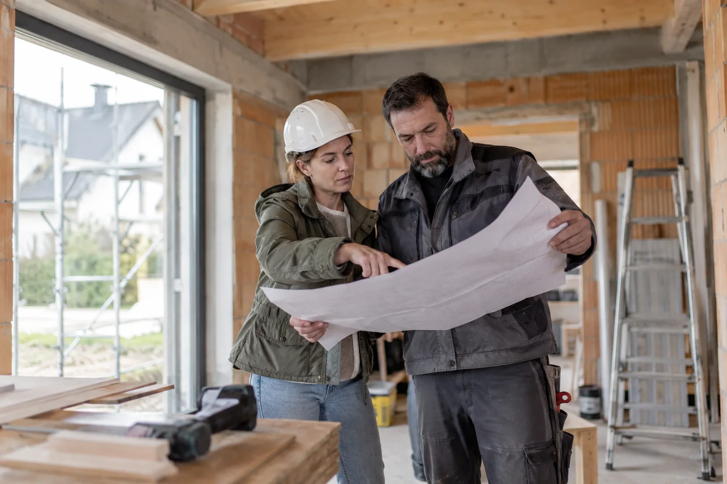 Baufinanzierung mit Eigenleistung – Ein Bauherr prüft die Arbeiten auf einer Hausbaustelle. Welche Eigenleistungen erkennt die Bank bei einer Baufinanzierung an? Materialkosten, Arbeitsstunden und Grenzen der Muskelhypothek. Baufinanzierung mit Eigenleistung: Ein Bauherr prüft die Arbeiten auf einer Hausbaustelle.